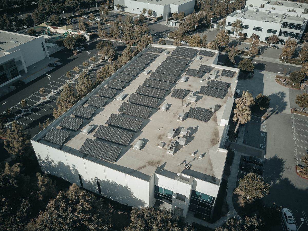 Aerial view of a commercial building with rooftop solar panels and surrounding palm trees